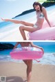 A woman in a bikini sitting on an inflatable ring on the beach.