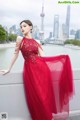 A woman in a red dress leaning against a wall.