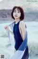 A woman in a black bathing suit holding a blue and white scarf.