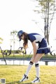 A woman in a blue and white uniform bending over on the grass.