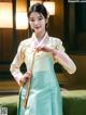 A woman in a green and yellow hanbok is posing for a picture.