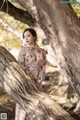 A woman in a floral dress leaning against a tree.