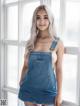 A woman in a denim dress posing by a window.