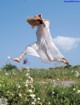 A woman in a white dress and straw hat jumping in the air.