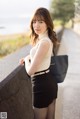 A woman in a white top and black skirt leaning against a wall.