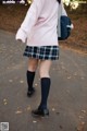 A woman in a pink sweater and plaid skirt walking down a road.