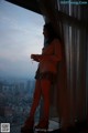 A woman standing in front of a window looking out at the city.