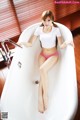 A woman in a white shirt and pink panties sitting in a bathtub.