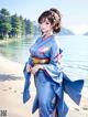 A woman in a blue kimono standing on a beach.