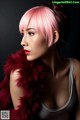 A woman with pink hair wearing a red fur stole.