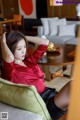 A woman in a red shirt and black skirt sitting on a green chair.